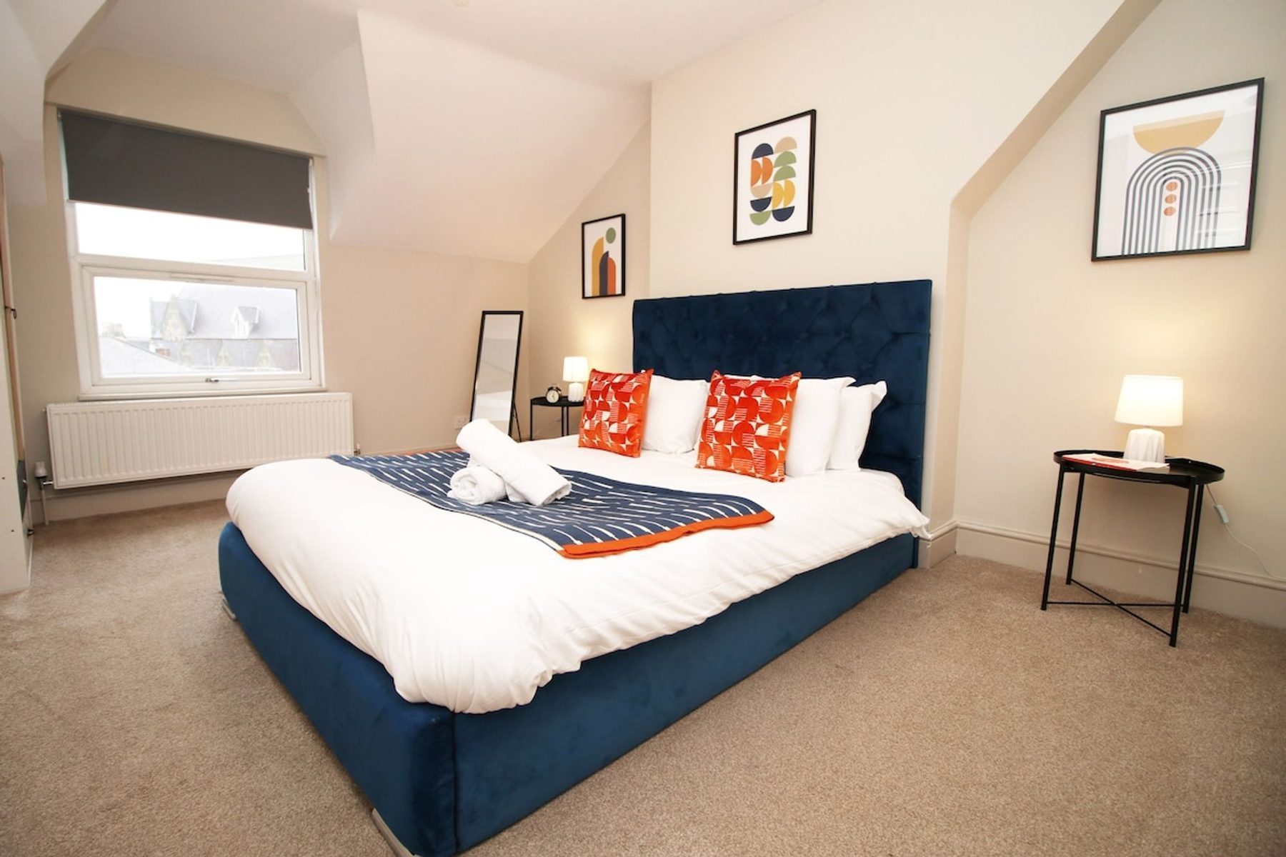 A freshly made bedroom in an EKLiving apartment in Cardiff, navy headboard and folded towels on the bed