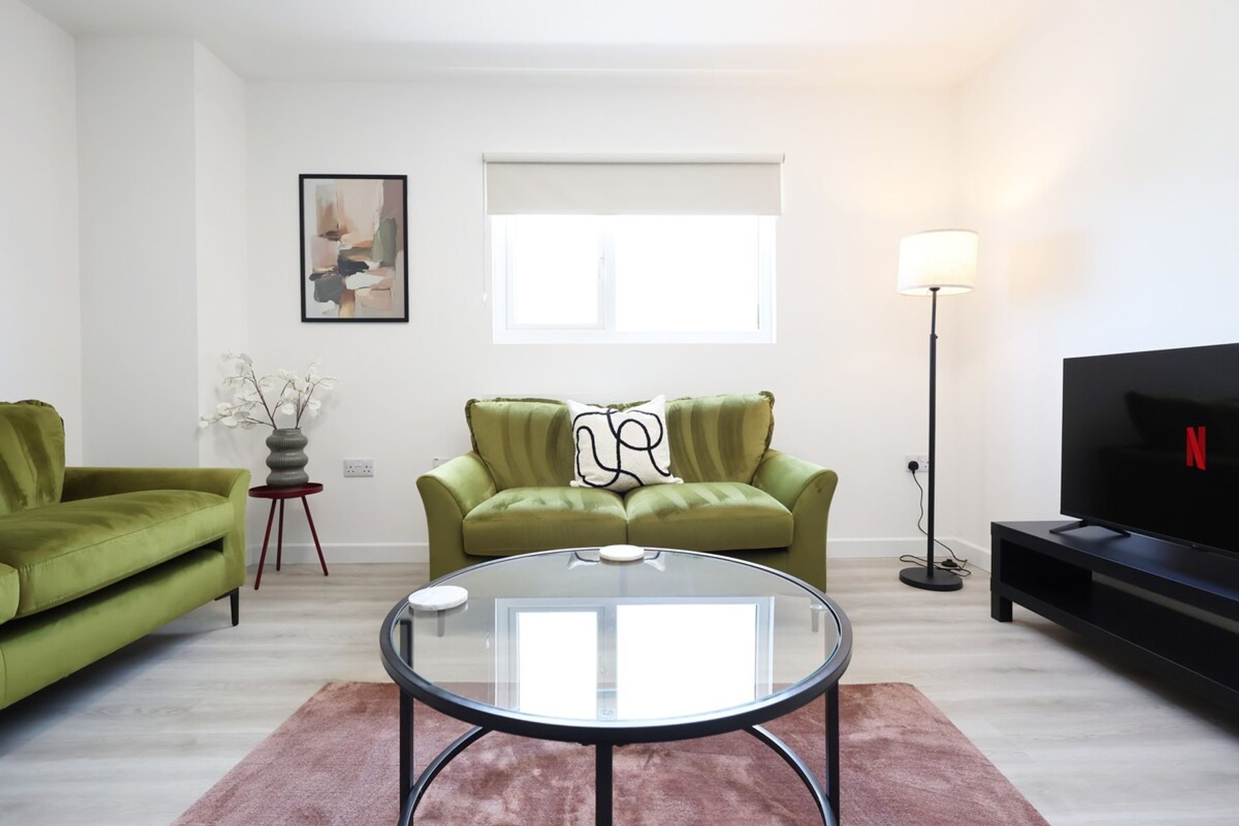 The living room of an EKLiving apartment in Bridgend town centre: green velvet sofas, a glass coffee table and a pink rug