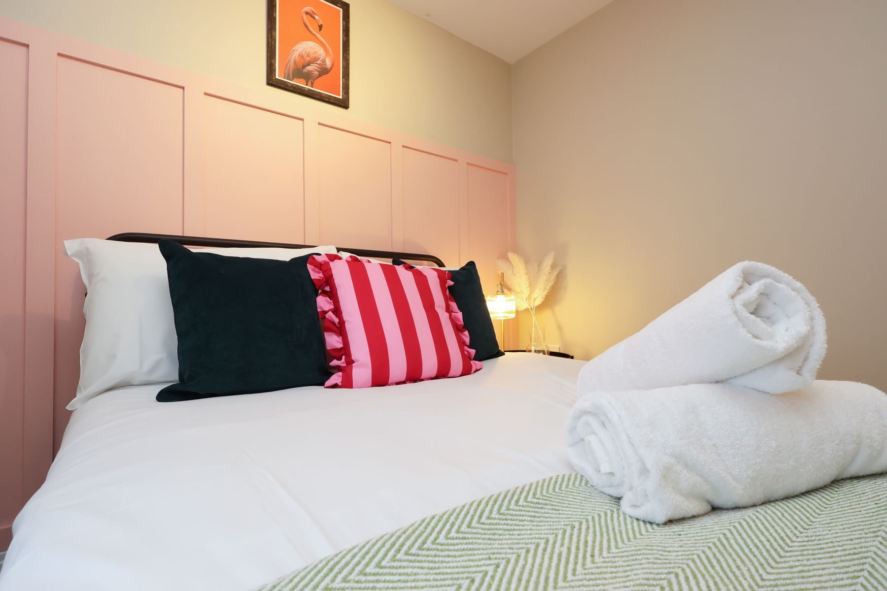 A bedroom in an EKLiving home in Bristol: a pink panelled wall and a double bed with striped cushions and rolled towels