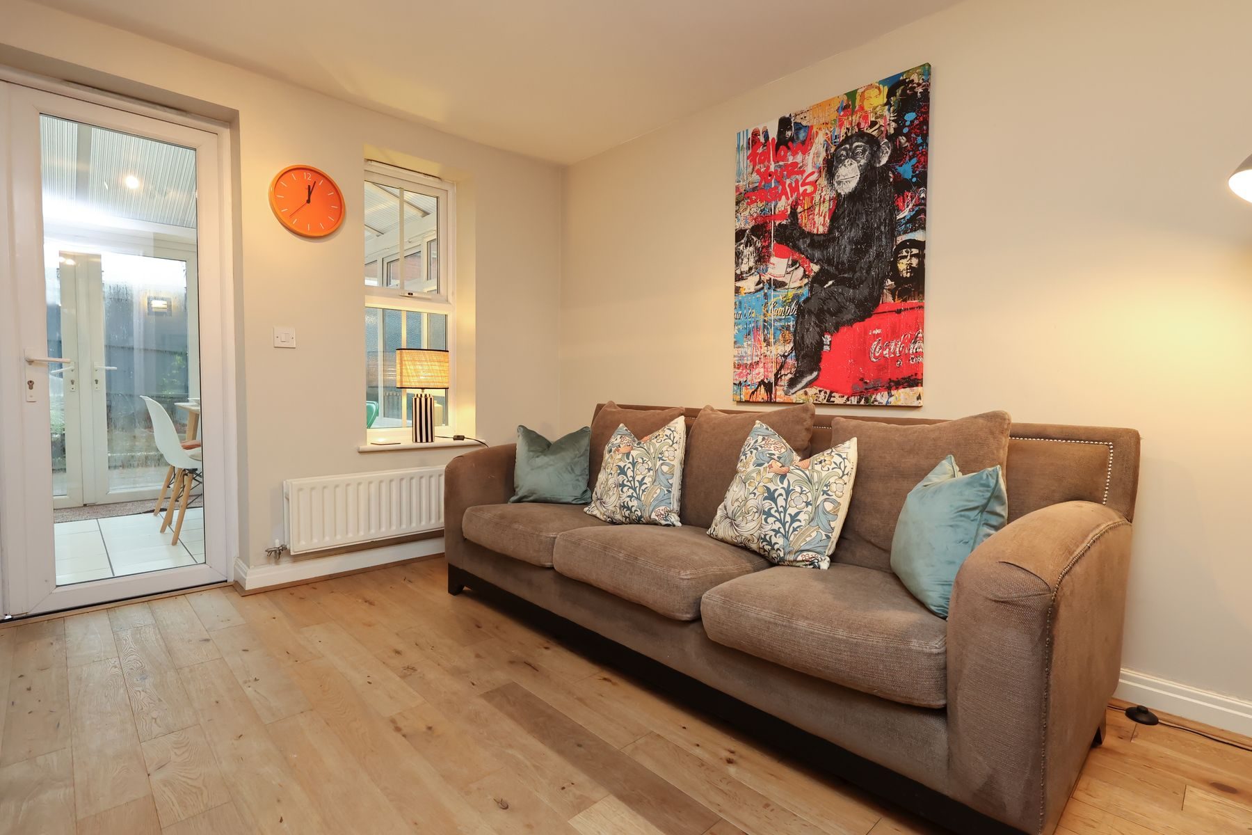 The living room of an EKLiving home in Redfield, Bristol: a brown sofa with patterned cushions, bold wall art and glazed doors to a garden room