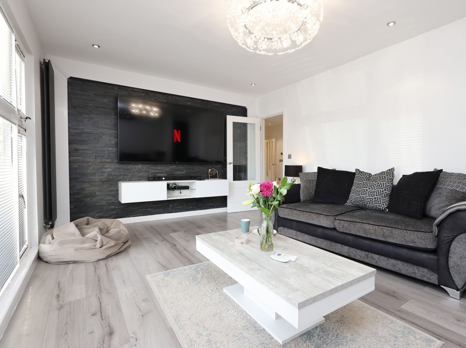 The lounge of an EKLiving house in Swansea: slate feature wall with a wall-mounted television, grey sofa, chandelier and a coffee table with fresh flowers