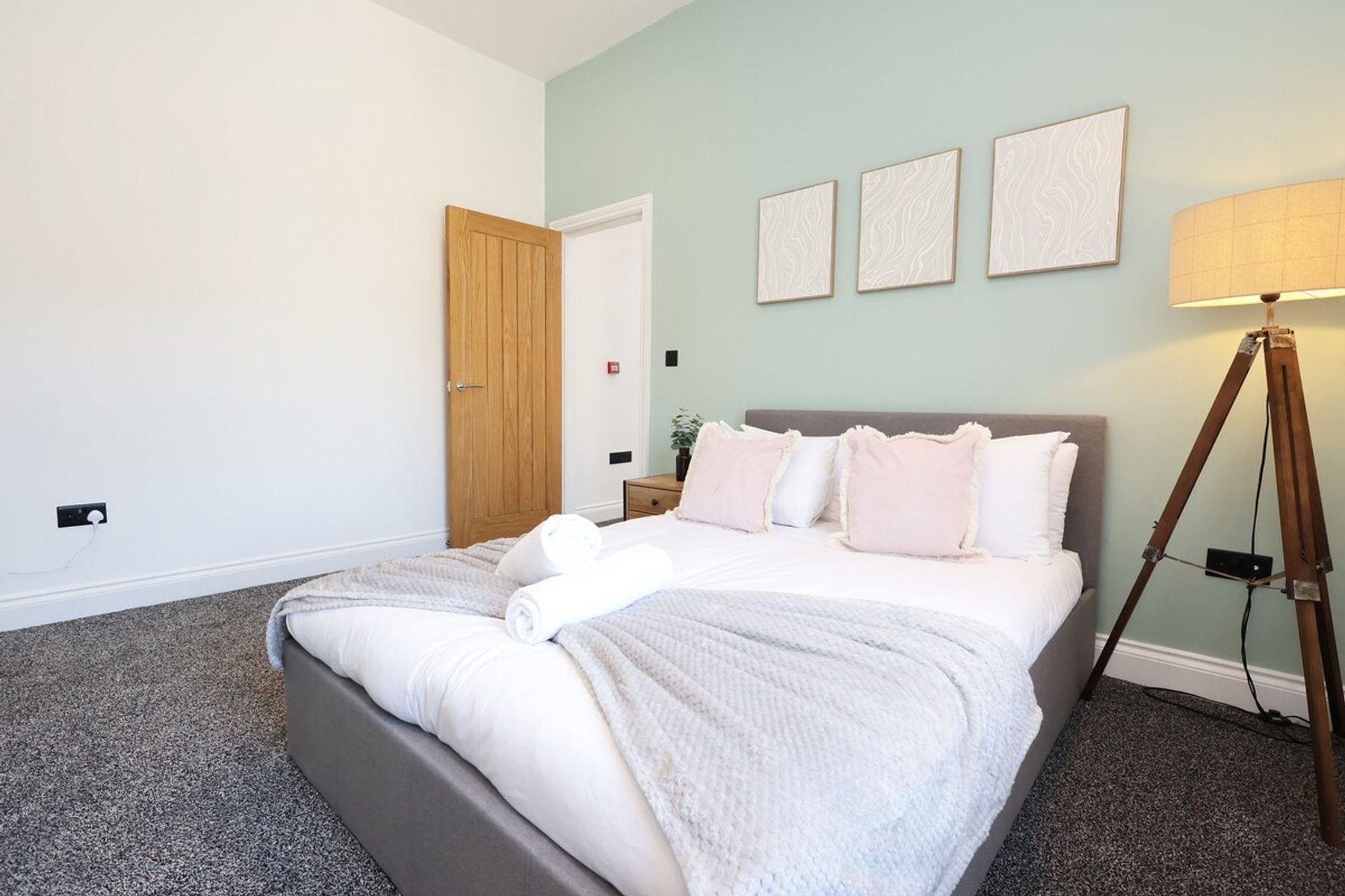 A bedroom in an EKLiving shared house in Swansea: double bed, sage walls and a tripod lamp