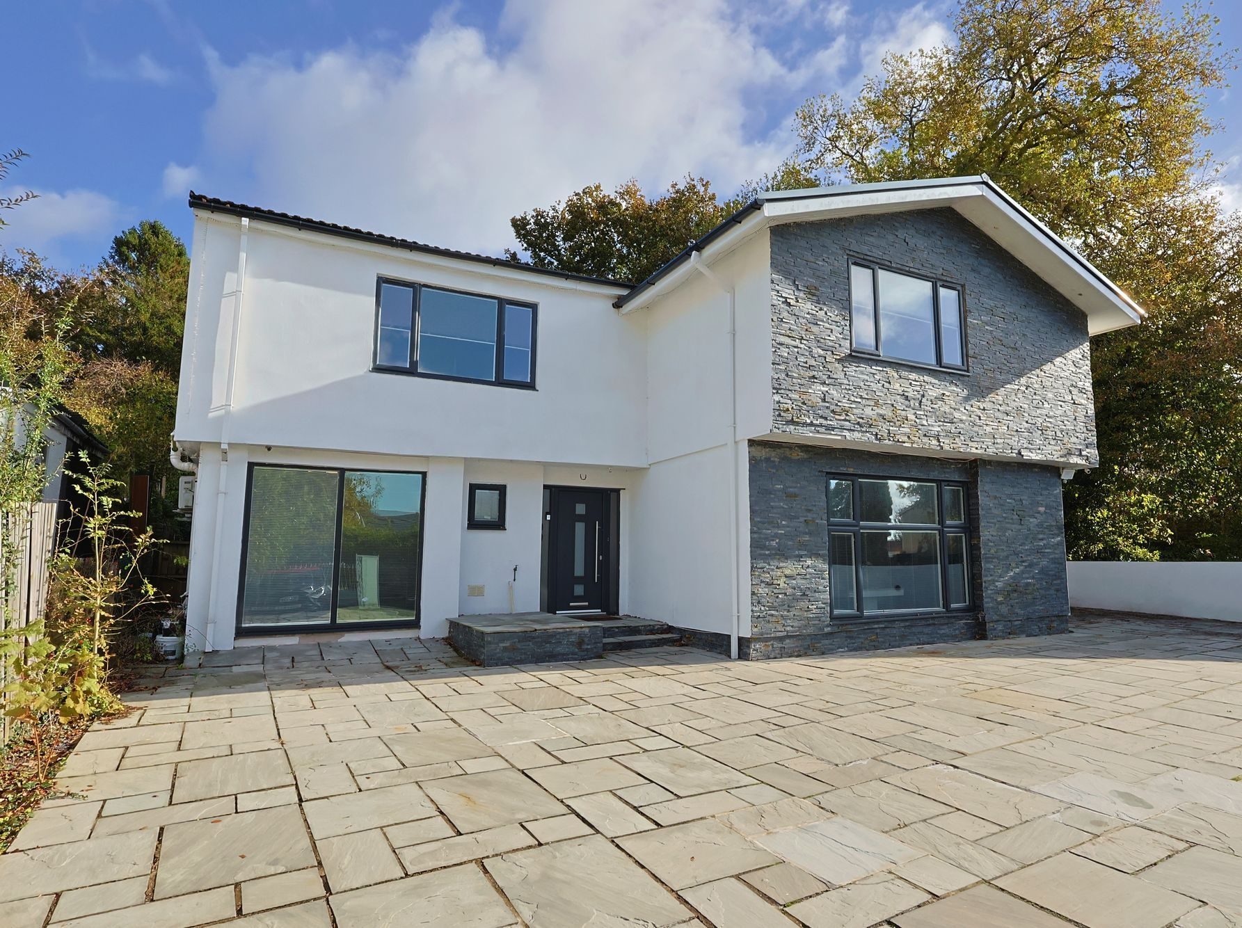 The front of a modern detached EKLiving house in Swansea, white render and slate cladding under a blue sky