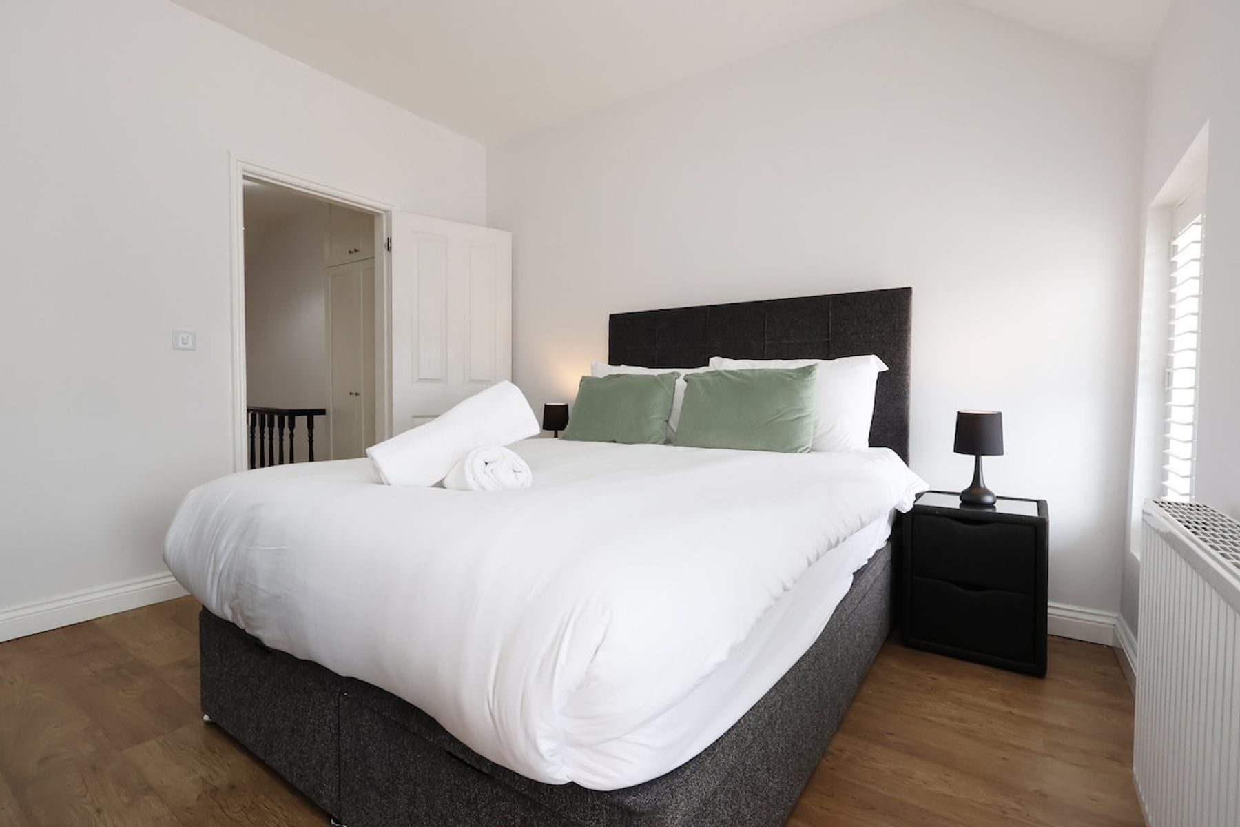 A bedroom in an EKLiving house in Pontypool: a double bed with white linen, sage cushions and a dark headboard